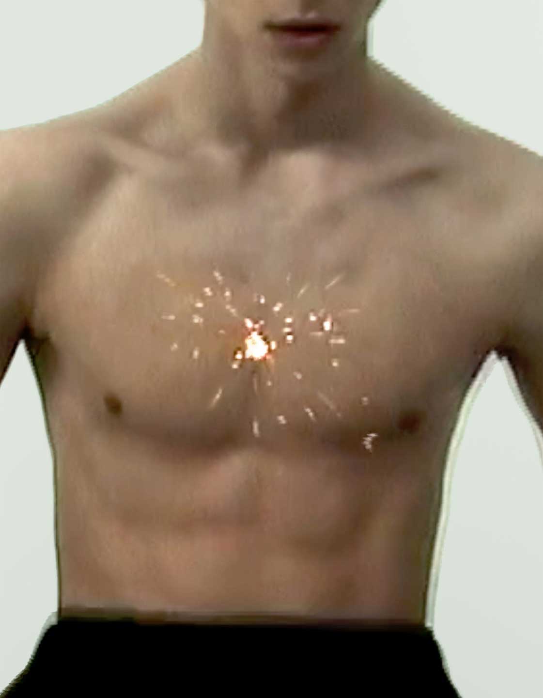 Sandro SS26 black trousers — close-up shot of Serkan Deniz's bare torso, lit with a sparkler effect at the center of his chest, radiating outwards.