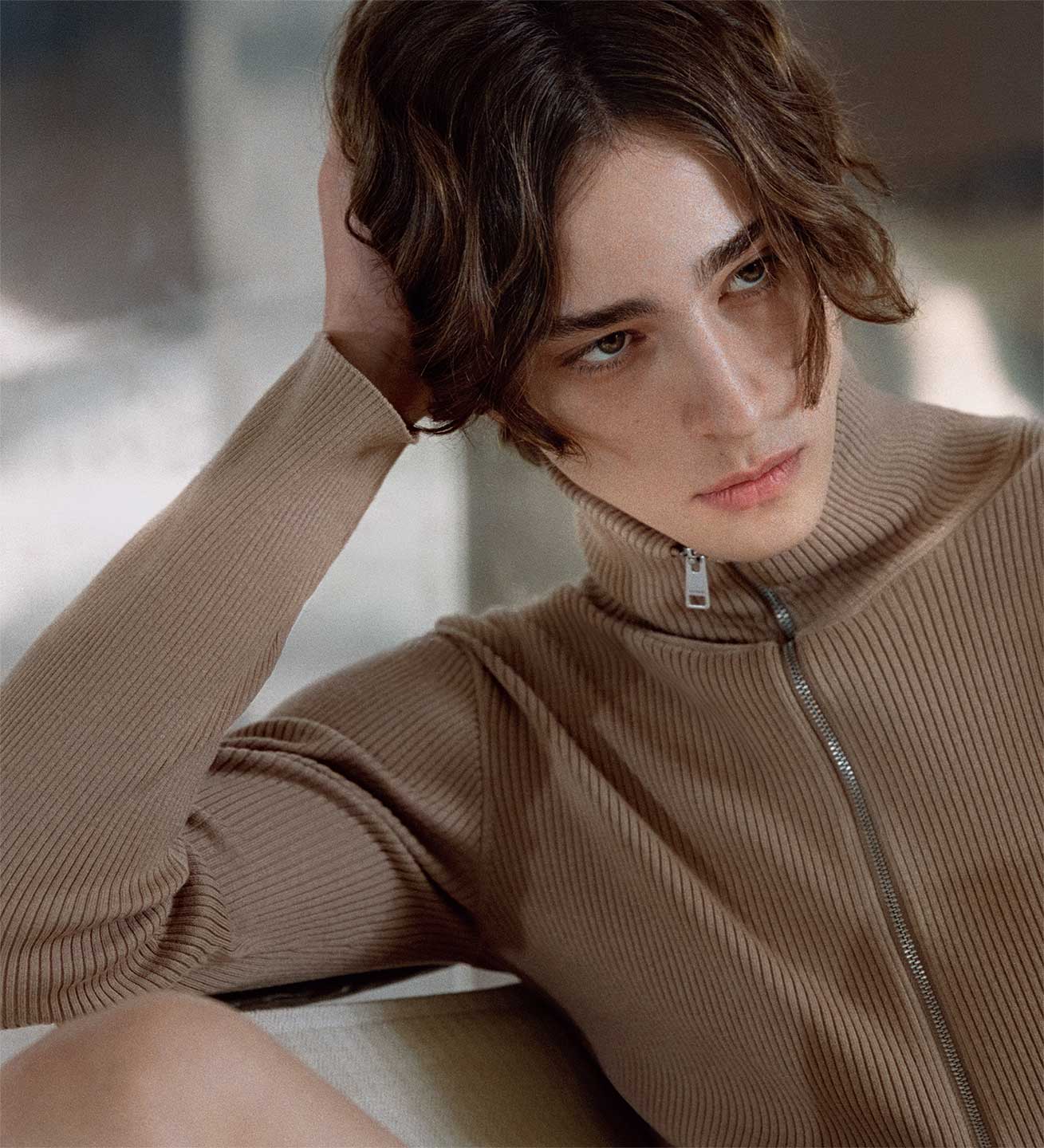 Serkan Deniz in a beige Sandro cardigan layered for Spring–Summer 2026, photographed on location with stark concrete geometry. Texture detail of a beige Sandro cardigan from SS26, knit surface shown in natural light.