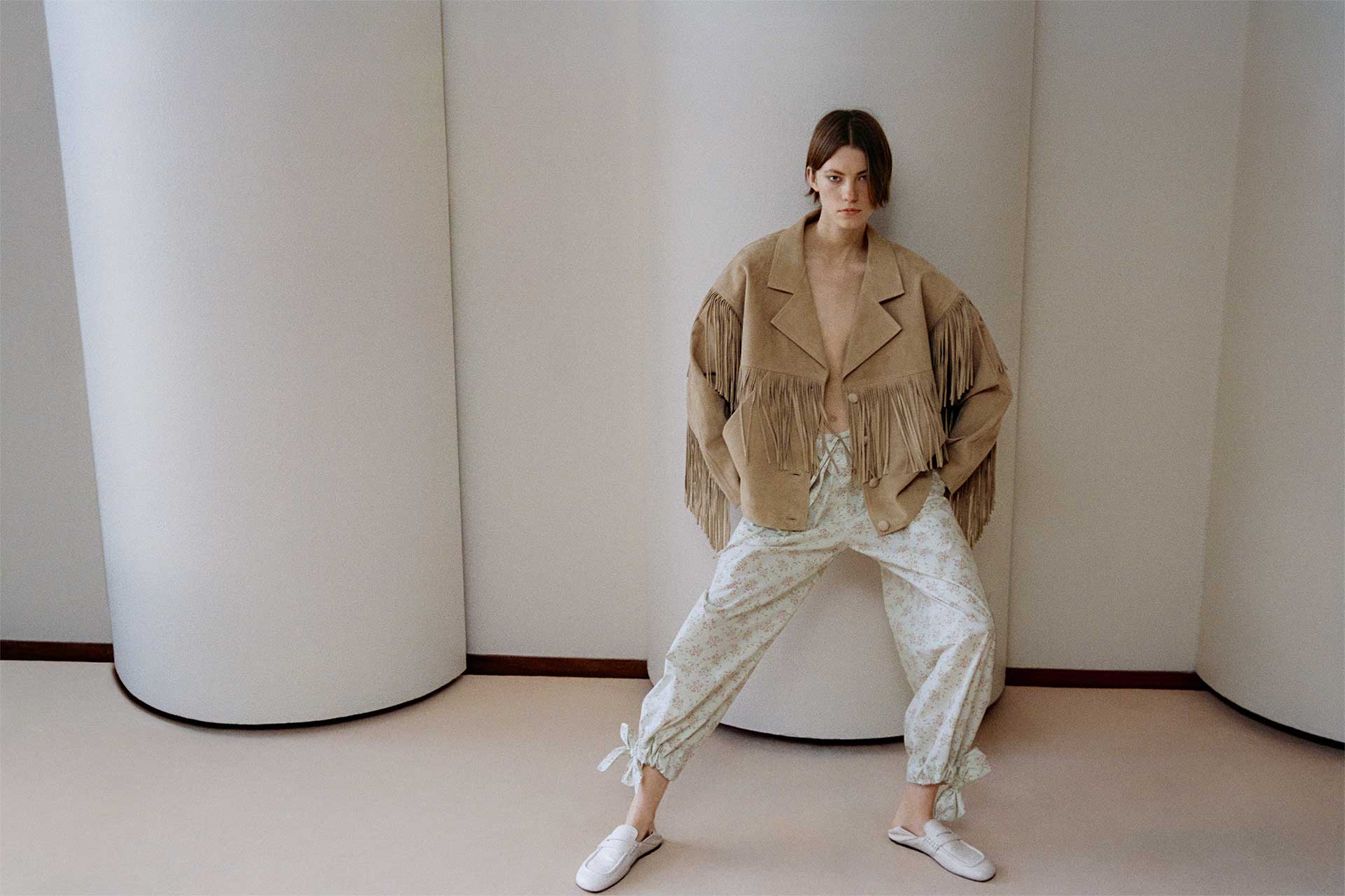 Dana Smith in a fringed suede leather jacket from Sandro SS26, movement emphasized against raw concrete forms.